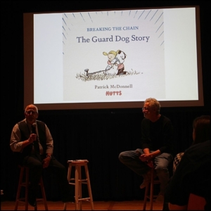 Curator Charles Viera on the left stool next to Patrick McDonnell on the right stool. On the screen behind them is the cover for "Breaking the Chain: the Guard Dog Story"